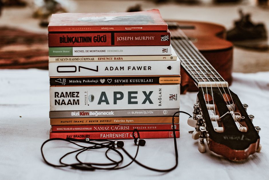 A collection of books stacked with an acoustic guitar and headphones, perfect for music and literature enthusiasts.