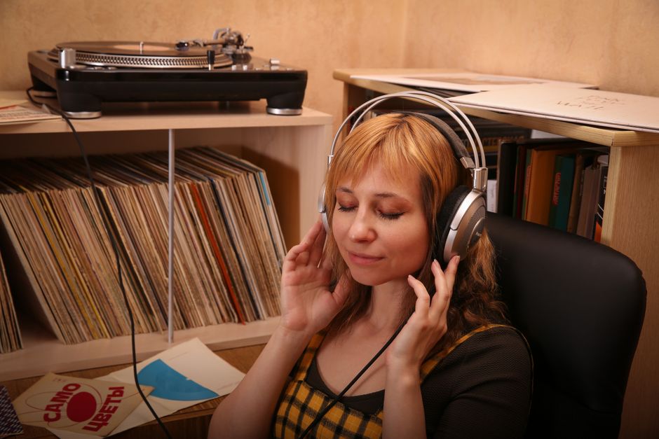 Serene woman enjoying music with headphones in a cozy room filled with vinyl records.