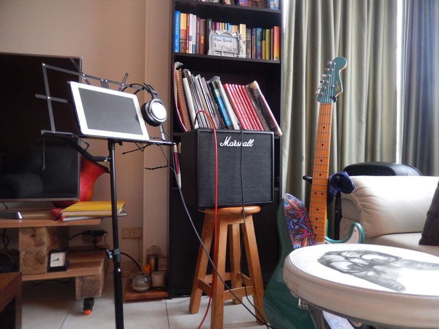 A music room featuring a guitar, amplifier, music stand with tablet, and bookshelf, perfect for musicians.