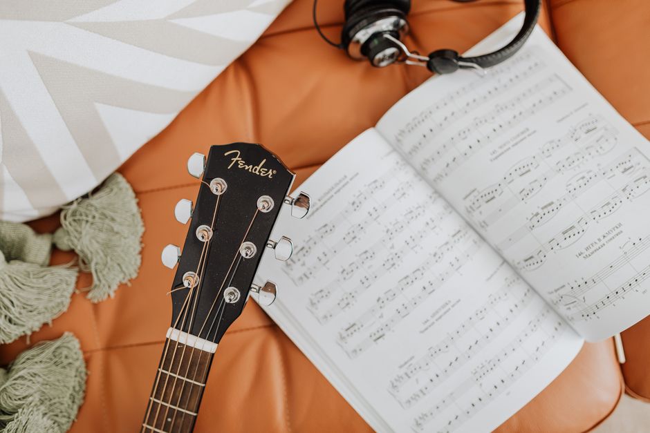Close-up shot of guitar headstock, sheet music, and headphones on a plush surface.